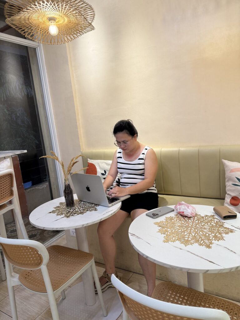 Jean Aguilar working remotely on her laptop in a cafe as a full time virtual assistant